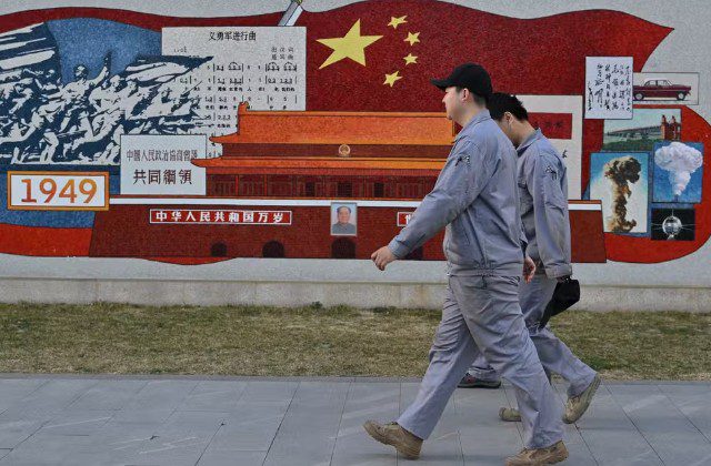 China anuncia execução de engenheiro condenado por espionagem Homens caminham diante de mural em Pequim, na China, em 19 de março de 2025. — Foto: Adek Berry/ AFP